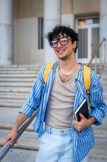 Young man with a backpack and a notebook, smiling while walking up the modern building stairs,