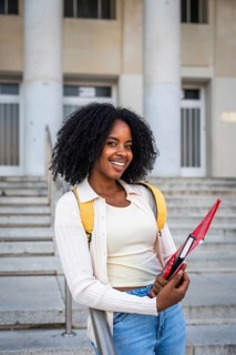 African american woman smiling while holding a notebook, wearing a backpack and standing in front
