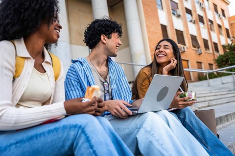 Group of diverse university students sharing a happy moment, laughing and eating lunch together on