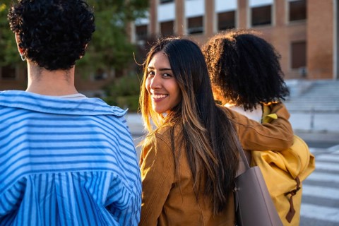 Diverse young adult students walking on a university campus during the day, one female student