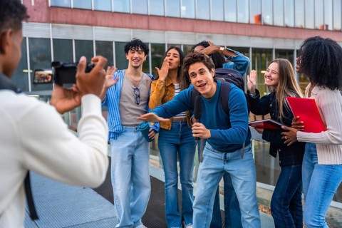 Group of happy diverse university students recording a video blog together with a camera, capturing