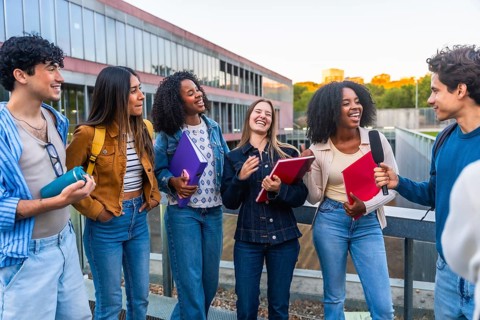 Group of happy young college students standing on a university campus getting interviewed by a