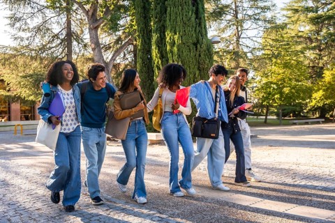 Group of young diverse students walking arm in arm, smiling and chatting while carrying books and