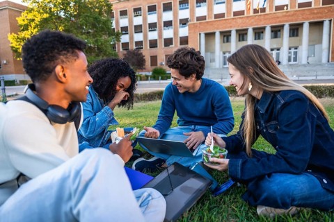 Group of diverse university students enjoying a refreshing outdoor lunch together on a grassy