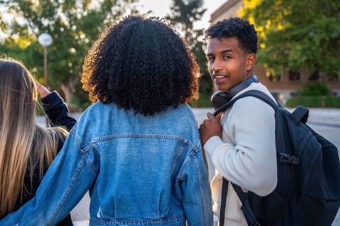 Three diverse young university students walking together on campus, the smiling man looking back at