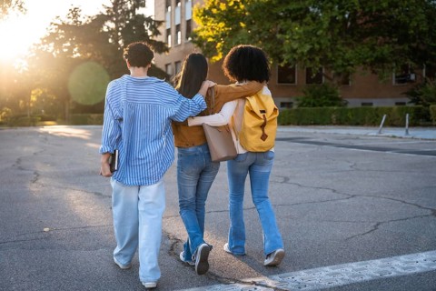 Diverse group of female students with arms around each other walking on a university campus at