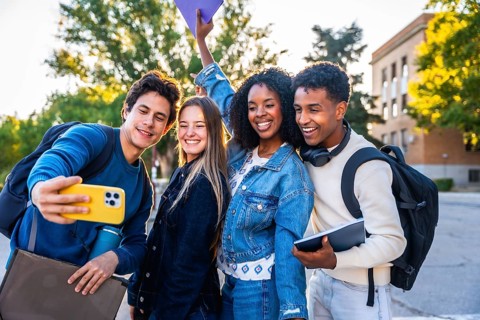 Happy diverse university friends smiling and taking a campus selfie with a smartphone, enjoying