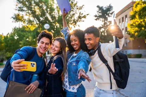 Diverse group of happy young students smiling and waving while taking a selfie together at a
