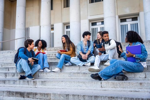 Diverse group of young students sitting on outdoor university stairs, actively communicating and