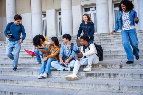 Diverse young students chatting, laughing and walking on wide stone campus steps by a university
