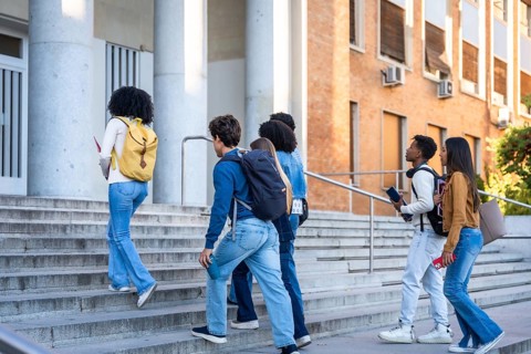 Group of multi ethnic students with backpacks and books walking up the steps of a university