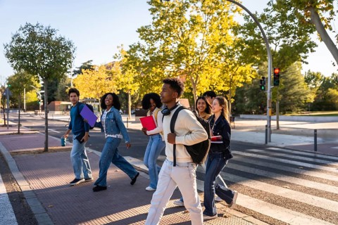 Multi ethnic group of university students walking across a campus crosswalk, smiling and chatting