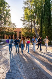 Group of diverse university students hurrying with textbooks and backpacks on a cobblestone path,
