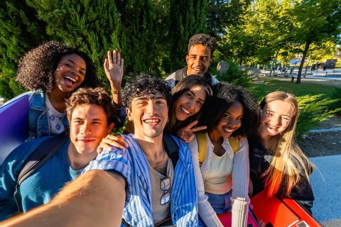 Group of happy multicultural young adult friends smiling and posing for a selfie while standing