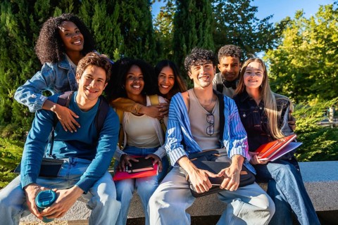 Diverse group of happy young male and female university students sitting outdoors on campus,