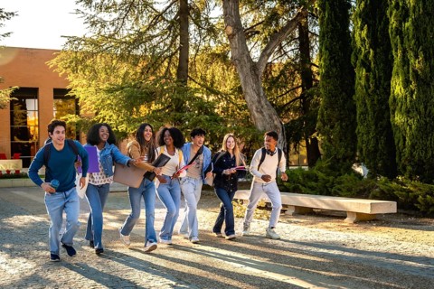 Diverse group of happy university students walking and talking together on campus, carrying books