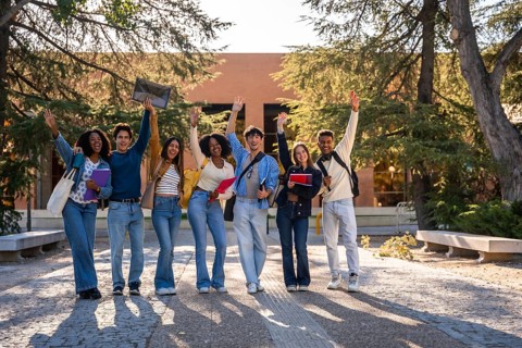 Group of diverse young university students happily standing in front of a campus building, smiling
