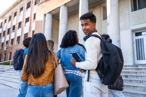 Group of diverse young university students with backpacks and books walking up the steps towards a