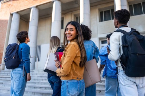 Group of young diverse students walking up steps towards a university building, carrying backpacks