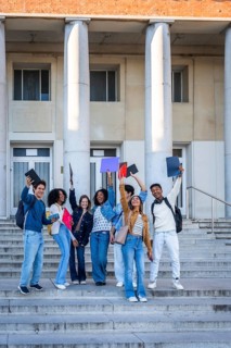 Diverse group of happy college students standing on the outdoor stairs of a university building,