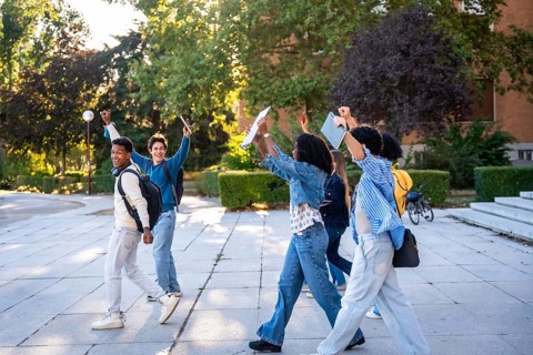 Diverse group of young university students walking on campus after classes, happily raising arms in
