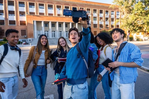 Diverse students standing together on a university campus, smiling and vlogging, capturing joyful