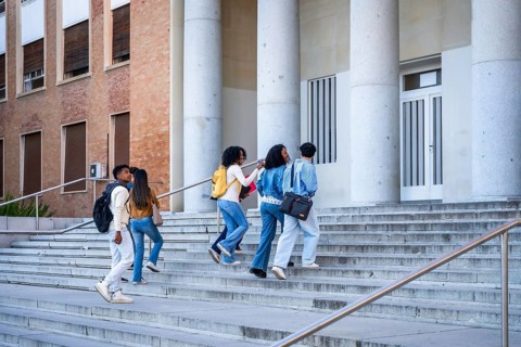 Diverse group of college students walking up wide outdoor steps toward a university building with