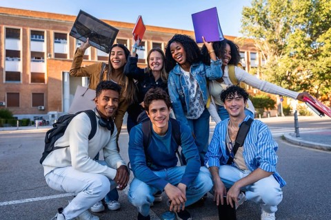 Diverse group of smiling university students on campus holding folders and backpacks, enjoying