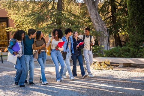 Group of multicultural university students walking and talking cheerfully together, carrying books,