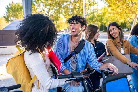 Young diverse students laughing and chatting with bikes and books on a sunny university campus,