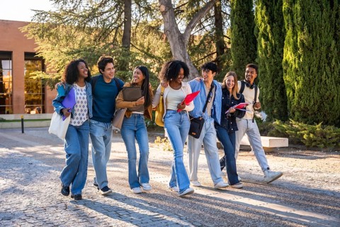 Diverse group of happy young university students walking together on campus, carrying books and