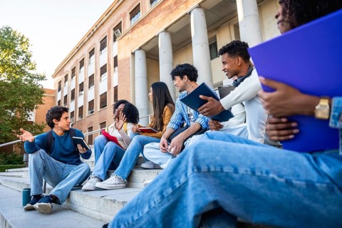 Group of diverse university students sitting on campus steps, discussing and sharing ideas in an
