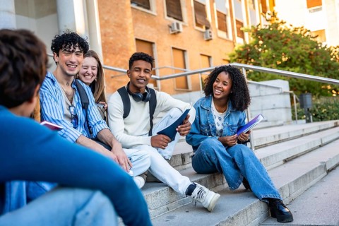 Diverse group of multiracial youth sitting on campus steps, engaging in conversation and smiling