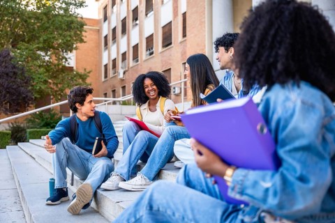Diverse group of university students sitting on campus steps, smiling and chatting confidently,