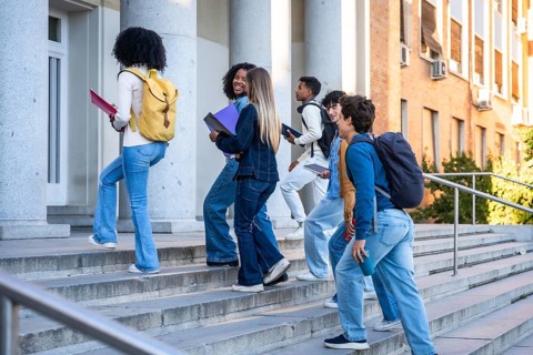 Diverse group of college students walking up campus stairs with backpacks and books, enjoying sunny