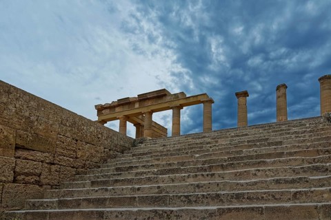 Ancient ruins with stone steps and columns of the Acropolis of Lindos under a dramatic sky,