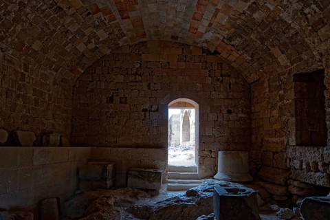 Dark room in ancient stone ruin with vault and doorway leading into the light, Acropolis, Lindos,