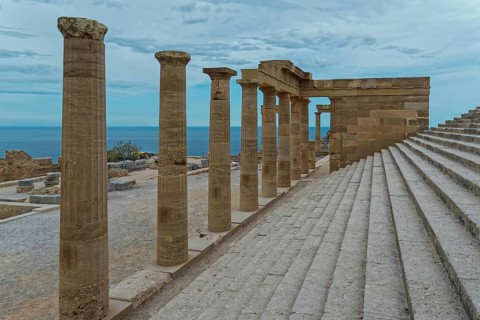 Ancient columns of the Acropolis of Lindos with a view of the sea and a staircase under a cloudy