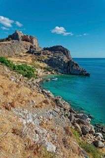 Steep cliffs Paulus Bay of Lindos over crystal clear blue water under a bright blue sky, Acropolis,