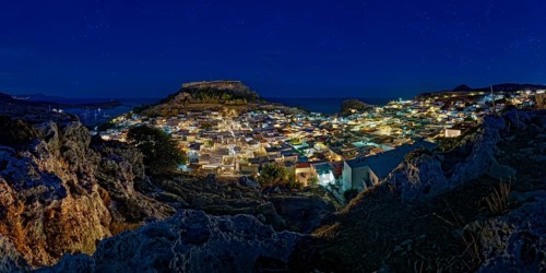 View of the illuminated town of Lindos with the ancient Acropolis under a starry sky with the sea,