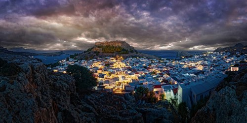 City view of Lindos with the ancient Acropolis at night with dramatic clouds, illuminated buildings