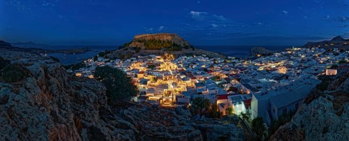 Panorama of picturesque Lindos and the ancient Acropolis at night with illuminated buildings and