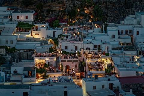 View of the illuminated roof terraces and restaurants of the town of Lindos and white houses that