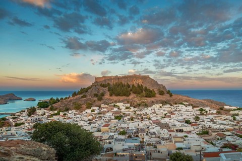 View of picturesque Lindos with the ancient Acropolis on a hill surrounded by the sea at sunset,