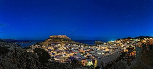 Wide angle photo of the city of Lindos with the ancient Acropolis in a clear night sky with glowing