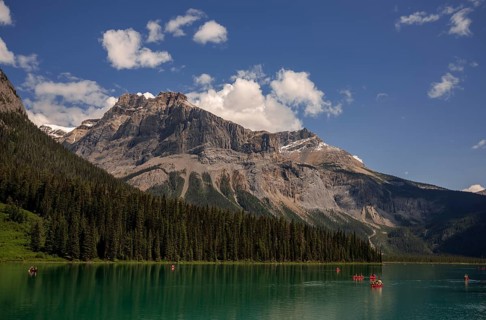Canoes navigating Emerald Lake surrounded by towering Canadian Rocky Mountains under a clear blue