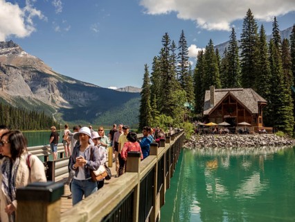 Tourists walking on a wooden bridge over Emerald Lake leading to a cabin, part of Emerald Lake