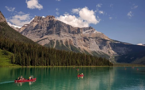Canoes on Emerald Lake surrounded by forest and the Canadian Rocky Mountains under a clear sky