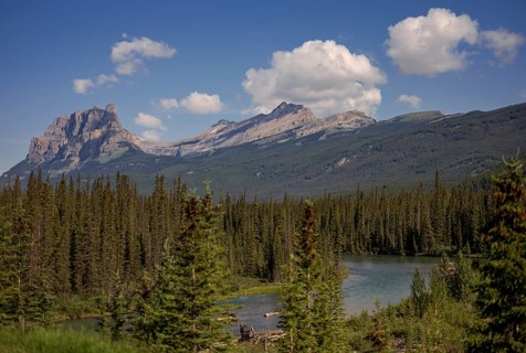 A tranquil mountain landscape of the Canadian Rocky Mountains with a lake, forest, and fluffy