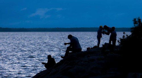 Silhouetted figures fishing and interacting by a lake at night in Ottawa, Ontario, Canada, North